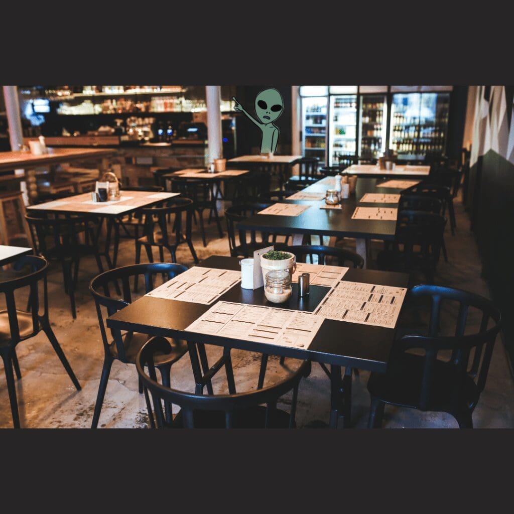 A Roswell Restaurant, vacant with black chairs and tables, menus at every place setting, an alien painted on the far wall
