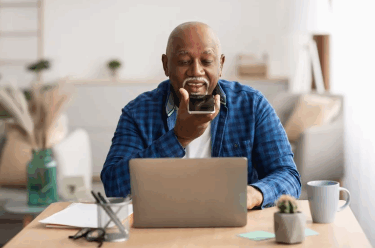 A man sits at a laptop, with his phone speaker pointed towards him, performing a zero-click search.