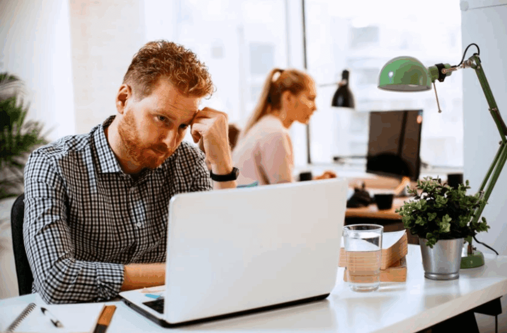 A man at a work desk with a laptop open, contemplating whether or not to Embrace AI