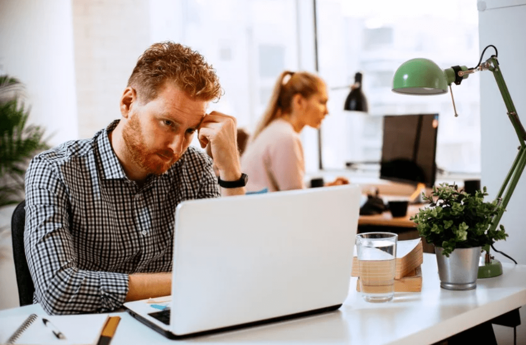 A man at a work desk with a laptop open, contemplating whether or not to Embrace AI